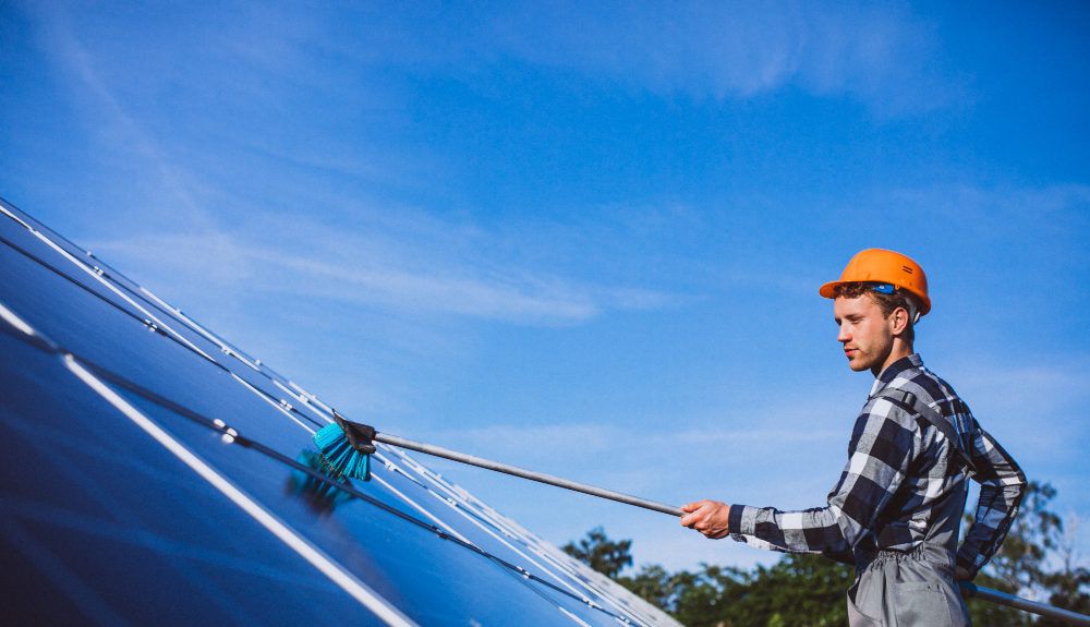 manutenzione dell'impianto fotovoltaico. Operaio che pulisce i pannelli solari con una spazzola telescopica