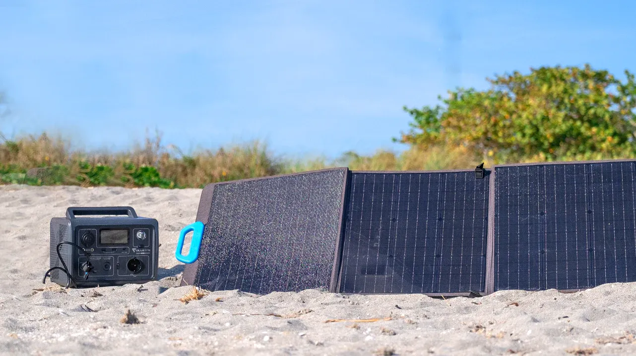 batteria  poggiata a terra, sulla sabbia, collegata a dei pannelli fotovoltaici portatili della Bluetti